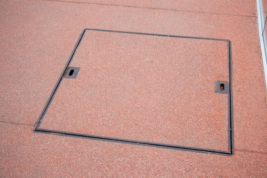 Rectangular metal utility cover in red granite pavement. Underground access point for maintenance or infrastructure in urban area. Real photo