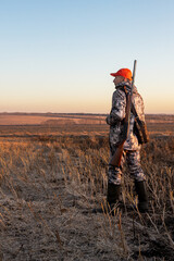  hunter with a gun walks across a field in autumn at sunrise.