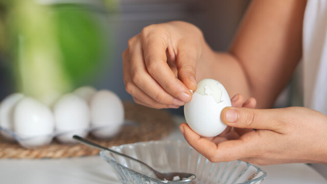 Close-up shot of woman hands peeling shell of boiled egg on the table