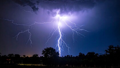 Lightning strike illuminates dark sky, trees in the foreground, creating a dramatic, high-contrast landscape