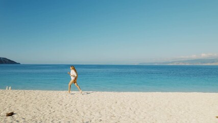 Woman jogging on secluded white pebble beach with blue sea in summer Greece