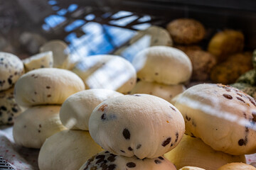 Homemade cheese rounds with dark specks displayed in a glass case, showcasing fresh dairy products, inviting textures, and artisanal craftsmanship in a vibrant market setting