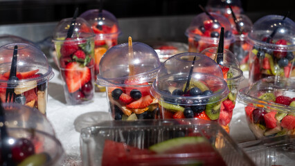 Colorful fruit cups filled with fresh strawberries, blueberries, kiwi, and watermelon, displayed in clear containers, perfect for healthy snacking and take-away options