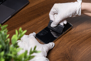 Person in white gloves carefully applies a transparent screen protector film onto a modern smartphone, ensuring optimal display protection and device longevity