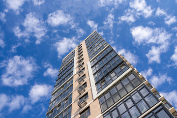 Modern residential building facade with glass windows and concrete panels against blue sky, perspective from below. For architecture, construction, building materials, real estate projects. Photo