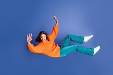 Joyful young woman in an orange sweater posing against a solid blue background with dynamic...