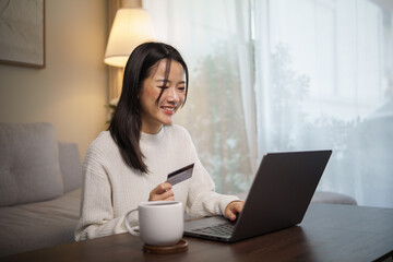 Young woman making online payment or e-commerce purchase with a credit card in a cozy living room.