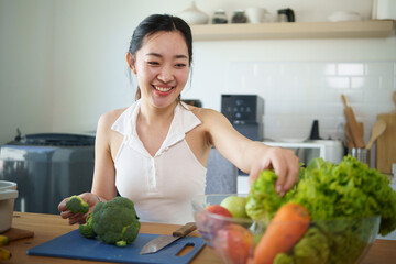 Cheerful woman cooking a healthy meal at home, selecting fresh vegetables from a bowl.