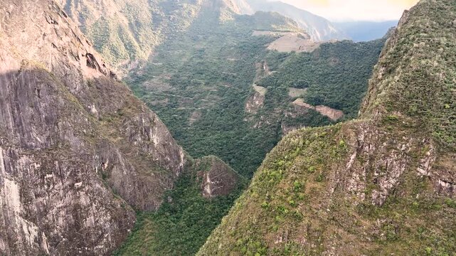 Drone flies past two mountains, including Huayna Picchu, revealing the ancient site of Machu Picchu in the distance surrounded by mist and fog