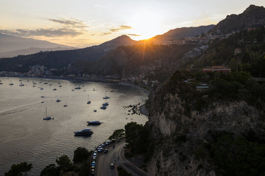 Aerial view of the sun's golden rays kissing the rugged coastline where the sea meets the cliffs, Taormina, Sicily, Italy.
