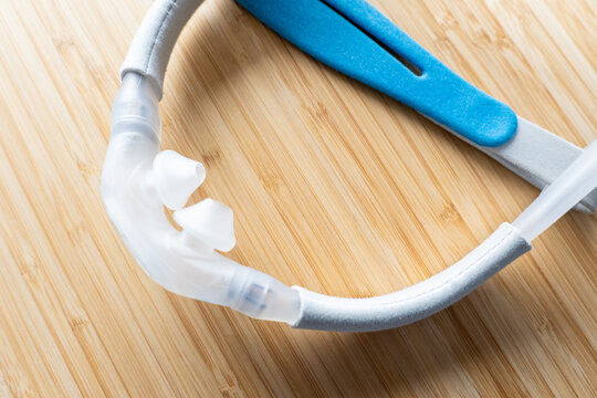 A nasal pillow CPAP mask and head straps shot over a wooden surface. The mask is used to give therapy to patiences who have been diagnosed with sleep apnea.