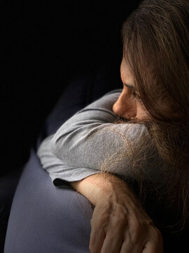 Woman in despair looking helpless, depressed and lost in thoughts seating in the dark room.