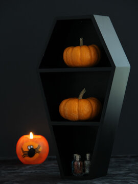 Halloween decorations in a spooky black coffin with pumpkins and a decorative orange lighted candle beside it with a dark background with copy space.