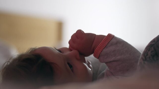 Baby lying on bed sucking thumb peacefully with soft daylight across face showing calm innocence comfort and early self soothing instinct in quiet moment