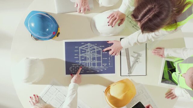 High angle view of engineers analyzing blueprints and digital devices at round table. Concept of architecture workflow, planning, and multidisciplinary teamwork in building design.