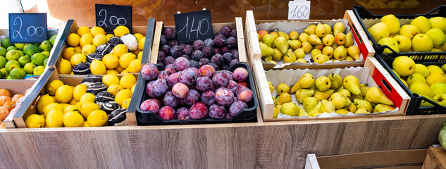 Organic fruit in crates at a farmers' market, lemons, plums, and pears on a stand.