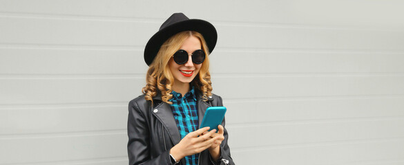 Stylish happy smiling modern young woman with phone, girl holding smartphone in black hat, jacket