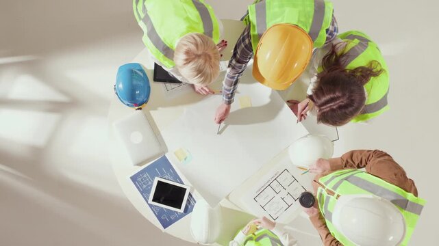 Top down view of architects discussing sticky notes and floor plans on table. Concept of idea exchange, design coordination, and modern teamwork in construction workflow.
