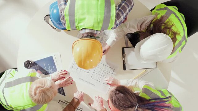 Zoom in overhead shot of engineers exchanging ideas over blueprints and technical diagrams. Concept of communication, teamwork, creative problem solving in construction and design process.