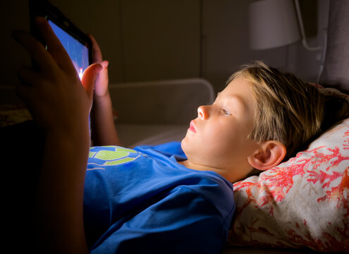 Little boy watching cartoons on iPad in bed at bedtime. Technology concept.
