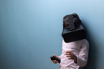 Asian little girl wearing VR headset and holding controller for playing and learning on blue wall background, concept of virtual reality education, metaverse, and future digital innovation.