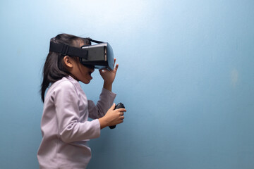 Happy little girl using VR headset and controller exploring immersive metaverse experience, concept of digital learning, virtual education, and futuristic technology for kids.