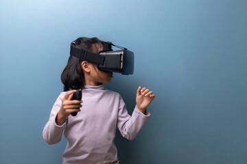 A young Asian girl wearing a virtual reality headset and holding a controller, exploring immersive digital experience, concept of future technology, education and metaverse.