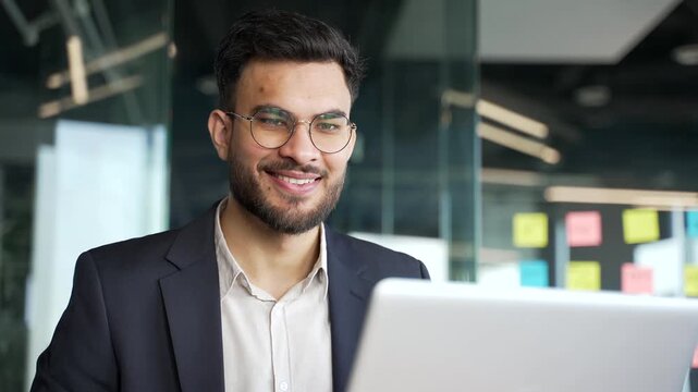 Happy businessman in a formal suit working on laptop computer sitting at workplace in business office. Smiling handsome worker banking, texting a client, chatting online. busy with a project. Close up