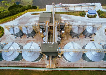 Aerial view of modern grain silos near river. Industrial agriculture storage facility surrounded by green fields and blue water. © pazyuk