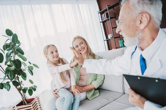 Playful family visit in living room scene doctor high fives girl and mom during friendly check up
