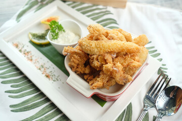 Golden crispy fried calamari rings with a side of sauce on a plate, close up shot