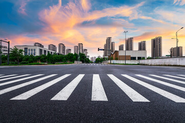 Obraz premium Empty city street intersection with crosswalk markings and modern residential buildings in the background at sunset.