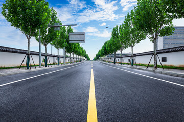 Empty straight asphalt road with green trees on both sides leading through a modern urban district.