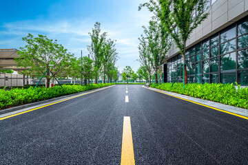 Empty asphalt road with yellow lines in a modern green business park with office buildings and trees.