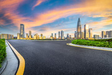 Empty curved asphalt road with a view of the modern city financial district skyline at sunset in Shenzhen.