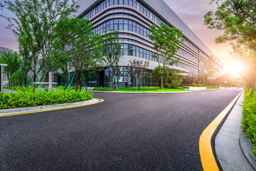 Empty asphalt road curving through a modern business park with contemporary office buildings at sunrise.