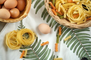 Pasta nests, eggs, and colorful rotini arranged in baskets. A delightful display of uncooked...