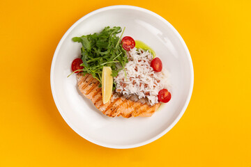 Salmon steak and rice in a plate on a yellow background.