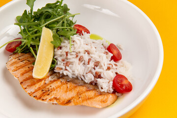 Salmon steak and rice in a plate on a yellow background.