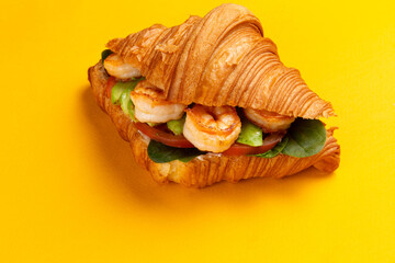 Croissant with shrimp and avocado on a yellow background.