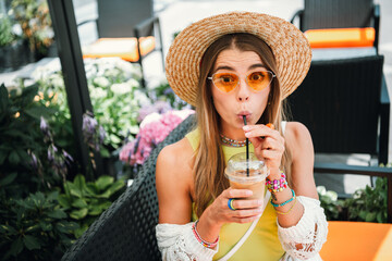 Young woman wearing a sunhat enjoys an iced drink at an outdoor cafe on a sunny day perfect for lifestyle travel and vacation imagery