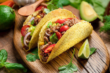 Mexican meat tacos or beef stuffed tortillas and lime slices near them on wooden serving board.