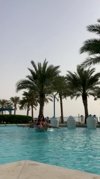 A girl floats on an inflatable ring in a pool. Relaxing in the pool against a backdrop of palm trees. A beautiful European girl in the pool.