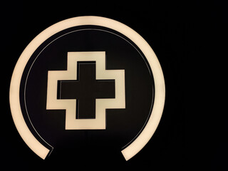 A glowing white cross symbol inside a circular frame against a dark background, representing health, aid, or medical assistance.