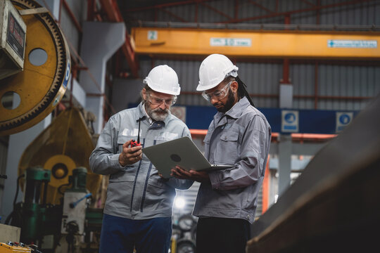 Two men in safety gear are looking at a laptop computer