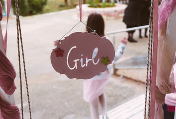 Pink decorative sign reading &ldquo;Girl&rdquo; hanging at a celebration entrance, with a child in the background, capturing a festive moment at what appears to be a baptism event.