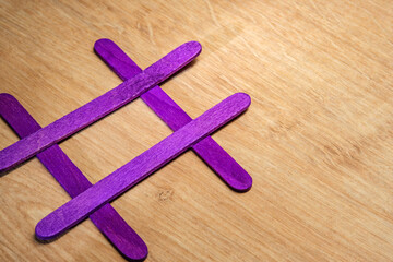 Creative arrangement of purple craft sticks forming a hashtag symbol on a wooden surface. Representing creativity, social media, hastag and handmade craft design concept with vibrant color contrast.