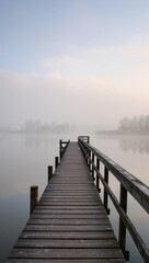 Naklejka premium A weathered wooden pier extends into a serene lake, shrouded in a soft, misty morning atmosphere, offering a tranquil scene.