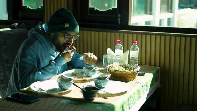 Man looks satisfied while eating a sandwich and paratha for breakfast at a caf&eacute; in Bhaderwah, Jammu and Kashmir, India.
