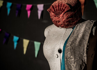 Vintage dress form draped with fabric and a decorative head-wra, set against dark background with colorful bunting, capturing a theatrical backstage or costume design atmosphere.